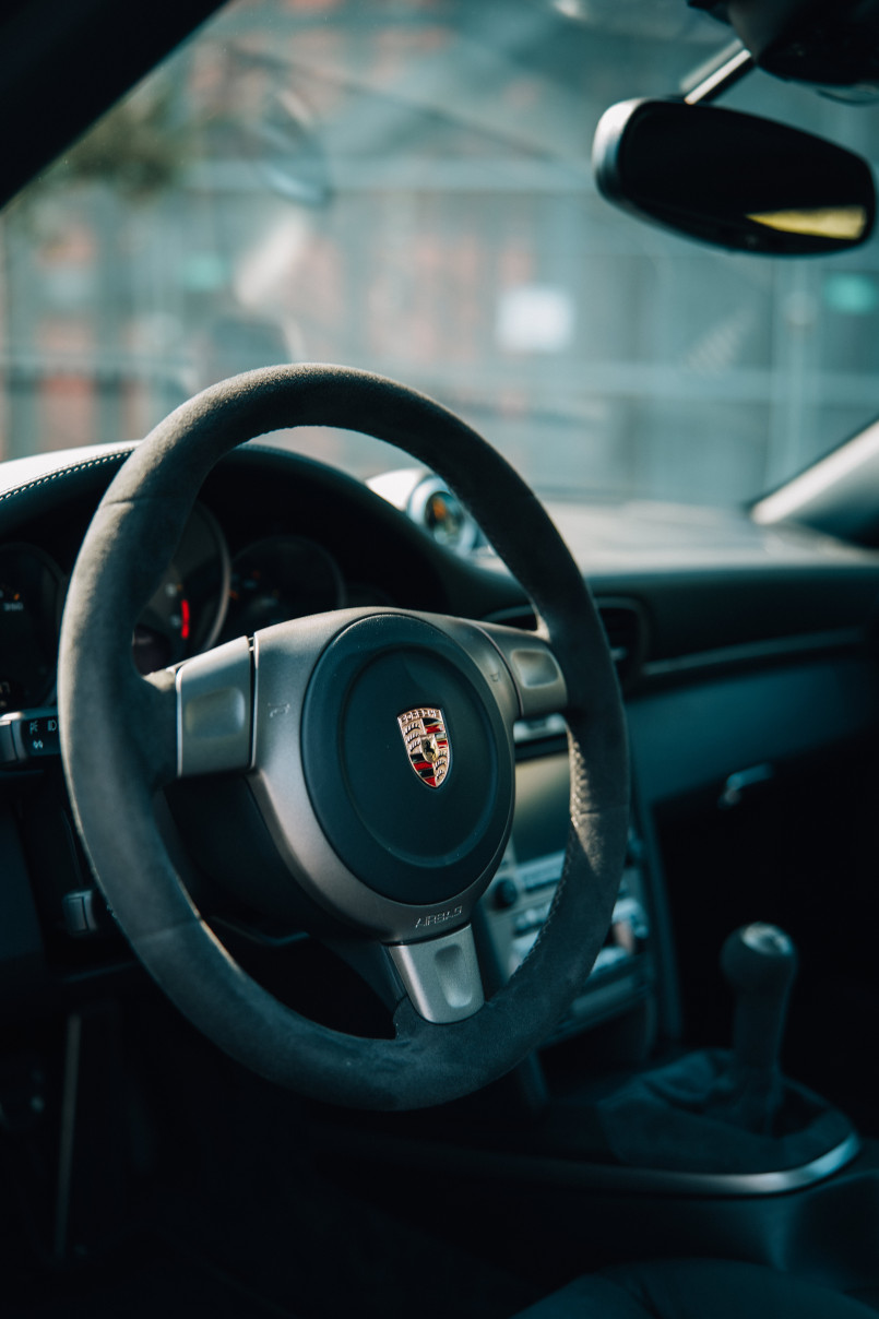 A close-up view of the interior of a Porsche, focusing on the steering wheel with the Porsche logo