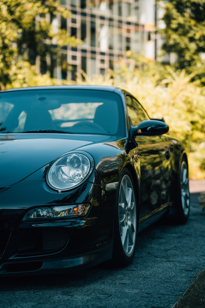 A black Porsche sports car parked outdoors, with trees and buildings in the background