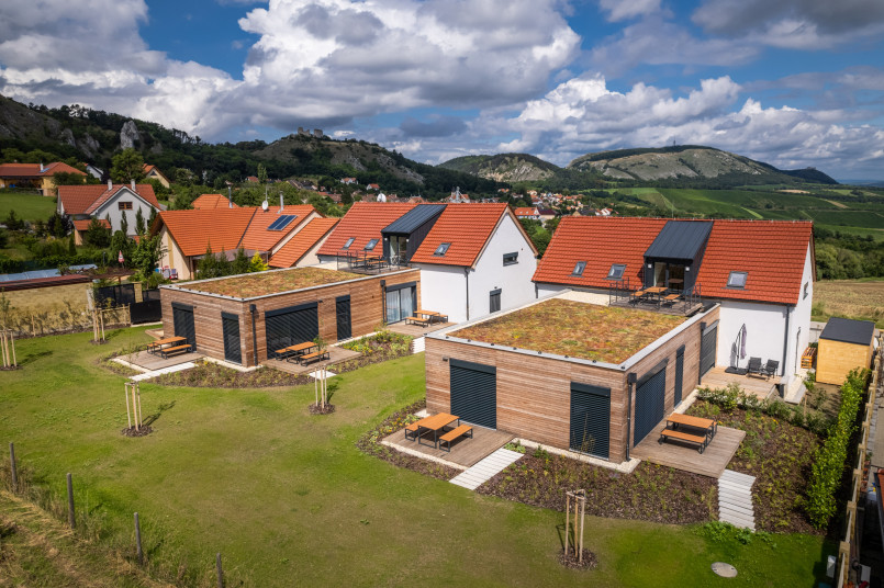 An aerial view of modern houses with red roofs and green terraces in a picturesque village, surrounded by mountains and hills