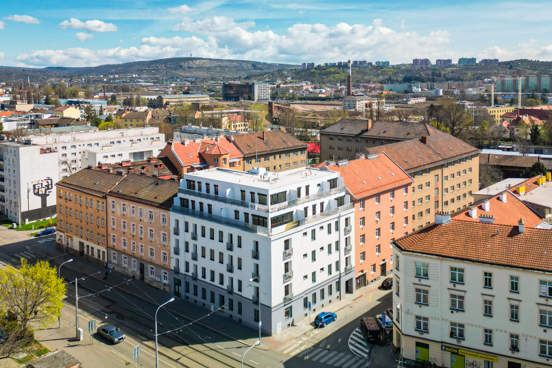 An aerial view of an urban area with modern and historic buildings, streets with cars, and hills and industrial buildings in the background